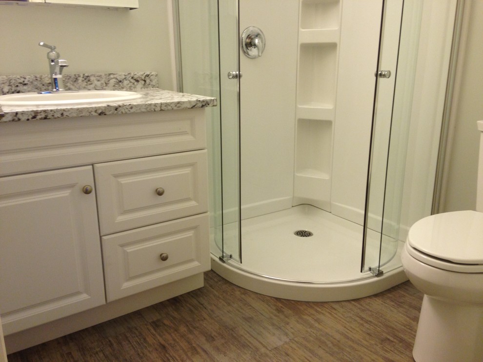 Esempio di una piccola stanza da bagno con doccia classica con ante con bugna sagomata, ante bianche, doccia ad angolo, WC a due pezzi, pareti grigie, pavimento in vinile, lavabo da incasso e top in laminato