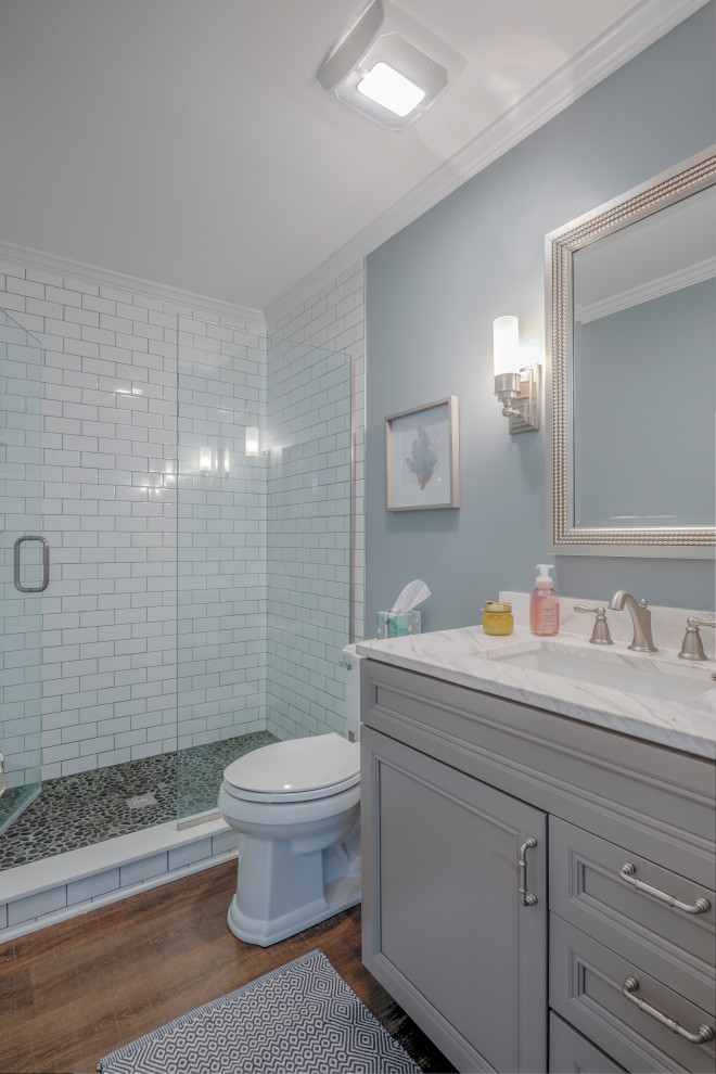 Example of a mid-sized beach style 3/4 white tile and subway tile medium tone wood floor alcove shower design in Other with recessed-panel cabinets, gray cabinets, a two-piece toilet, an undermount sink, marble countertops, a hinged shower door and white countertops