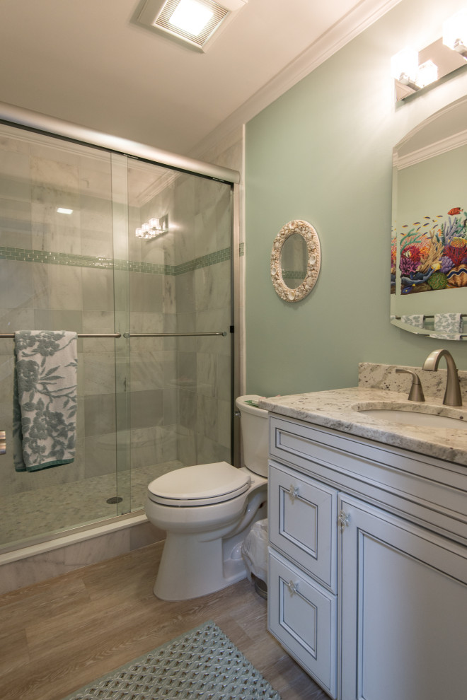 Maritim inredning av ett mellanstort badrum med dusch, med luckor med infälld panel, vita skåp, en dusch i en alkov, en toalettstol med separat cisternkåpa, marmorkakel, gröna väggar, vinylgolv, ett undermonterad handfat, granitbänkskiva och dusch med skjutdörr