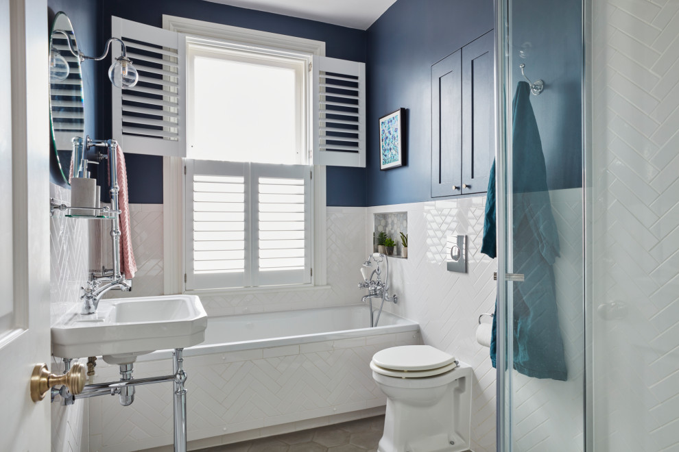 Cette image montre une salle de bain principale traditionnelle avec des portes de placard blanches, une baignoire posée, un carrelage blanc, un mur bleu, un lavabo de ferme, un sol gris, une cabine de douche à porte battante, un plan de toilette blanc, meuble simple vasque et meuble-lavabo encastré.
