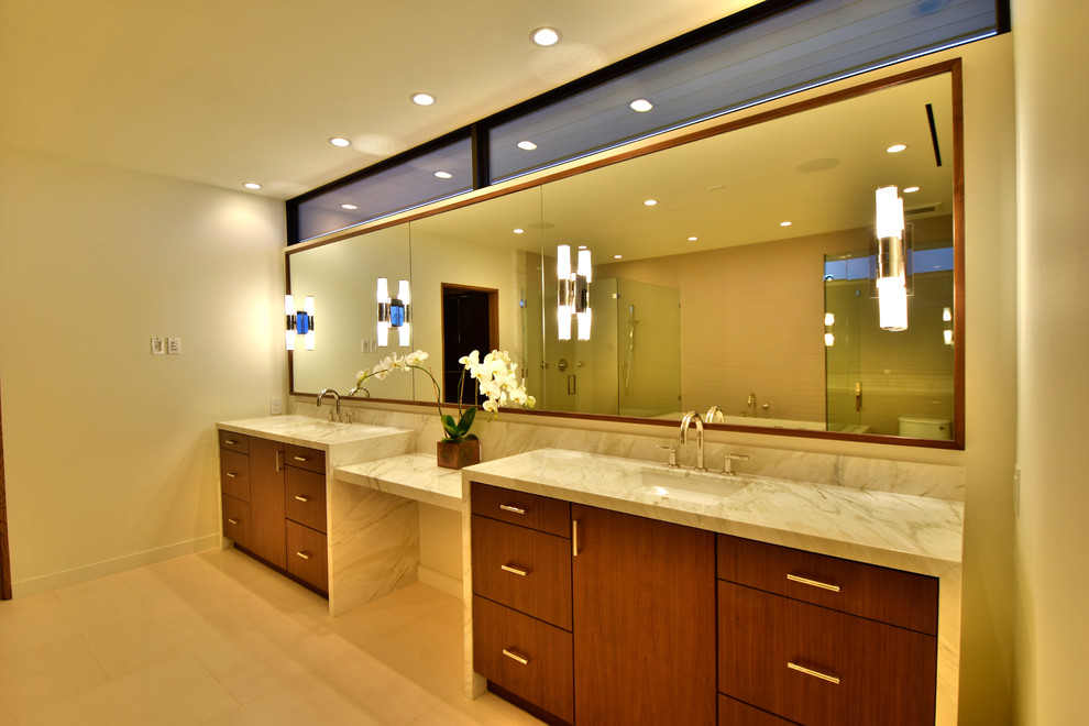 Cette image montre une grande salle de bain principale minimaliste en bois brun avec un placard à porte plane, un mur beige, un lavabo encastré, un plan de toilette en marbre et un sol beige.