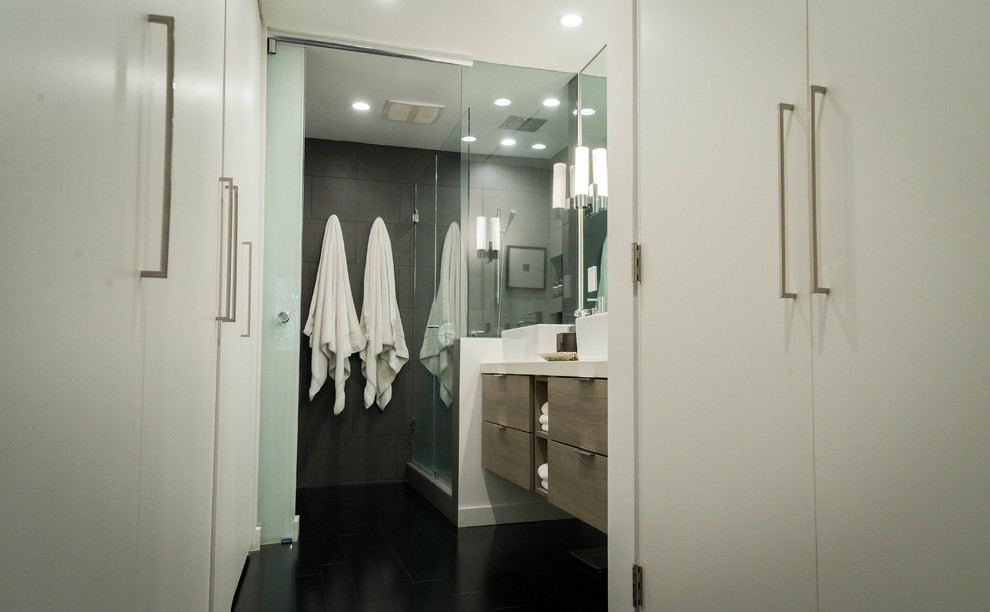 Alcove shower - mid-sized modern master black tile and porcelain tile dark wood floor and black floor alcove shower idea in Los Angeles with flat-panel cabinets, distressed cabinets, a wall-mount toilet, black walls, a vessel sink, solid surface countertops and a hinged shower door