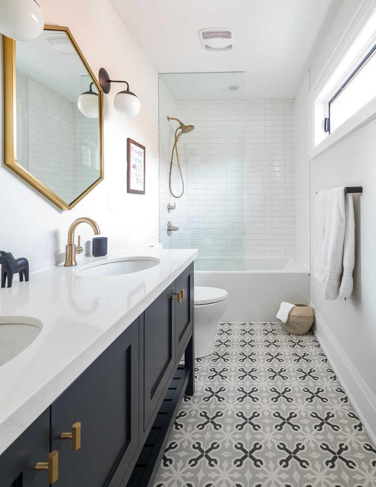 Cette image montre une salle de bain traditionnelle avec un placard à porte shaker, des portes de placard grises, une baignoire en alcôve, un combiné douche/baignoire, un carrelage blanc, un mur blanc, un lavabo encastré, un sol gris et un plan de toilette blanc.