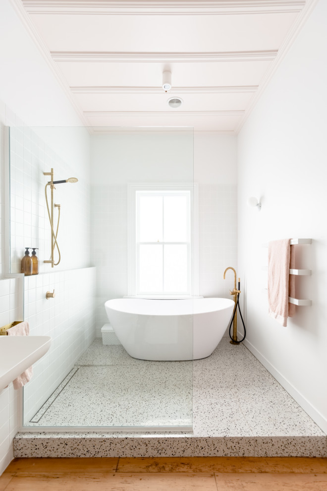 На фото: ванная комната среднего размера в стиле фьюжн с белыми фасадами, душем в нише, инсталляцией, белой плиткой, керамической плиткой, белыми стенами, полом из терраццо, подвесной раковиной, разноцветным полом и душем с распашными дверями с