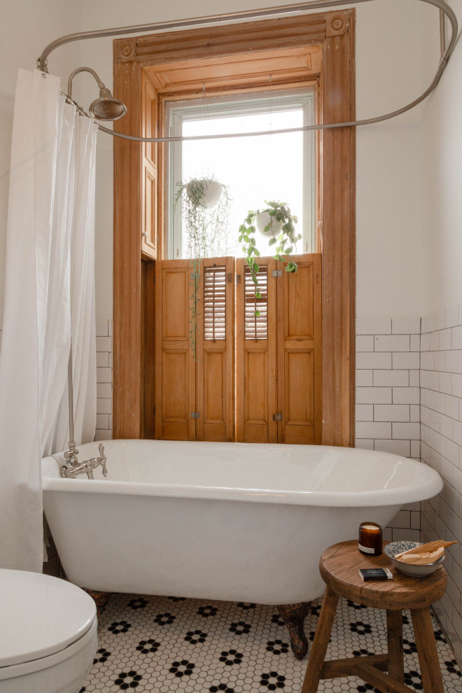 На фото: ванная комната в стиле кантри с ванной на ножках, душем над ванной, унитазом-моноблоком и белыми стенами с
