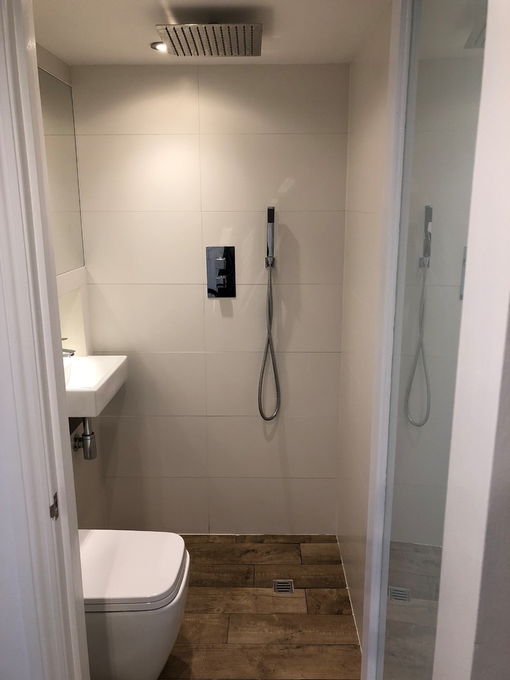 Design ideas for a modern ensuite wet room bathroom in London with a wall mounted toilet, white tiles, ceramic tiles, white walls, porcelain flooring, a wall-mounted sink and brown floors.