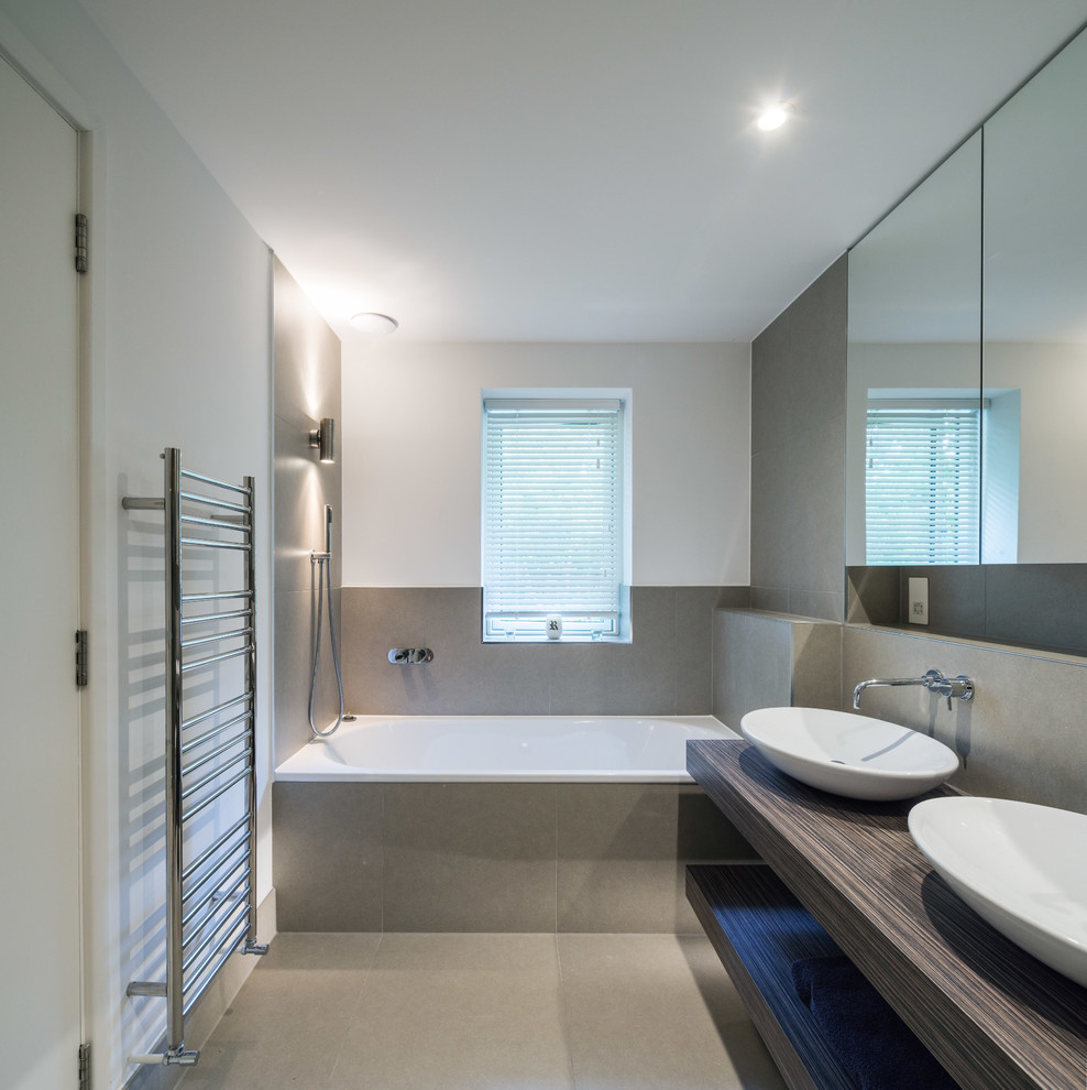 На фото: ванная комната среднего размера в современном стиле с открытыми фасадами, столешницей из дерева, накладной ванной, душем над ванной, серой плиткой, белыми стенами, темными деревянными фасадами и коричневой столешницей