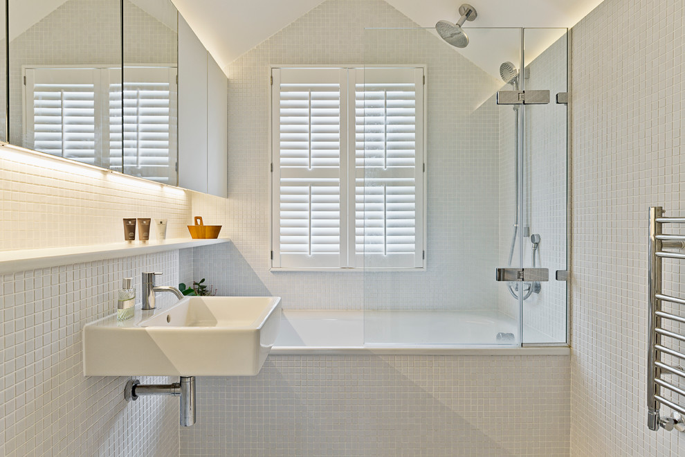 Foto på ett litet funkis badrum med dusch, med ett badkar i en alkov, en dusch/badkar-kombination, vit kakel, vita väggar, släta luckor, ett väggmonterat handfat och med dusch som är öppen