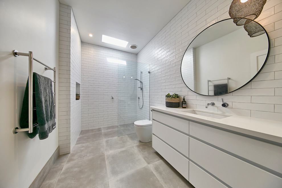 Стильный дизайн: ванная комната с плоскими фасадами, белыми фасадами, душем без бортиков, унитазом-моноблоком, белой плиткой, белыми стенами, душевой кабиной, врезной раковиной, серым полом, открытым душем и белой столешницей - последний тренд
