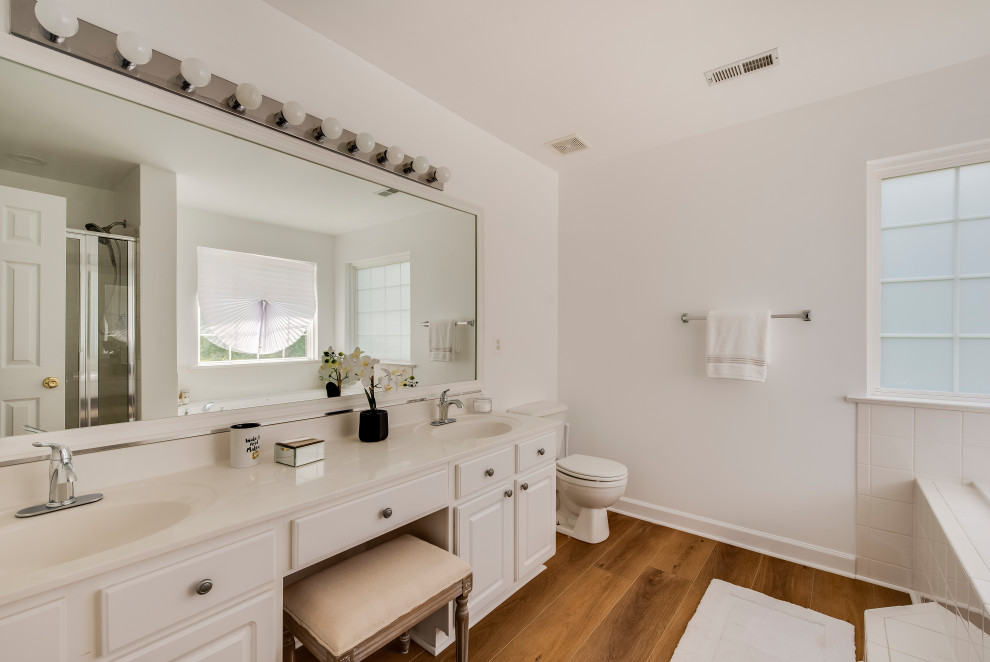 Photo of a large contemporary ensuite bathroom in Baltimore with white cabinets, a corner bath, vinyl flooring, yellow floors, white worktops, a built in vanity unit, a two-piece toilet, white tiles, ceramic tiles, white walls and an integrated sink.