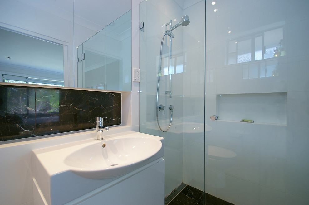 Inspiration for a medium sized contemporary ensuite bathroom in Sydney with a vessel sink, recessed-panel cabinets, white cabinets, solid surface worktops, a freestanding bath, a walk-in shower, a wall mounted toilet, white tiles, porcelain tiles, white walls and marble flooring.