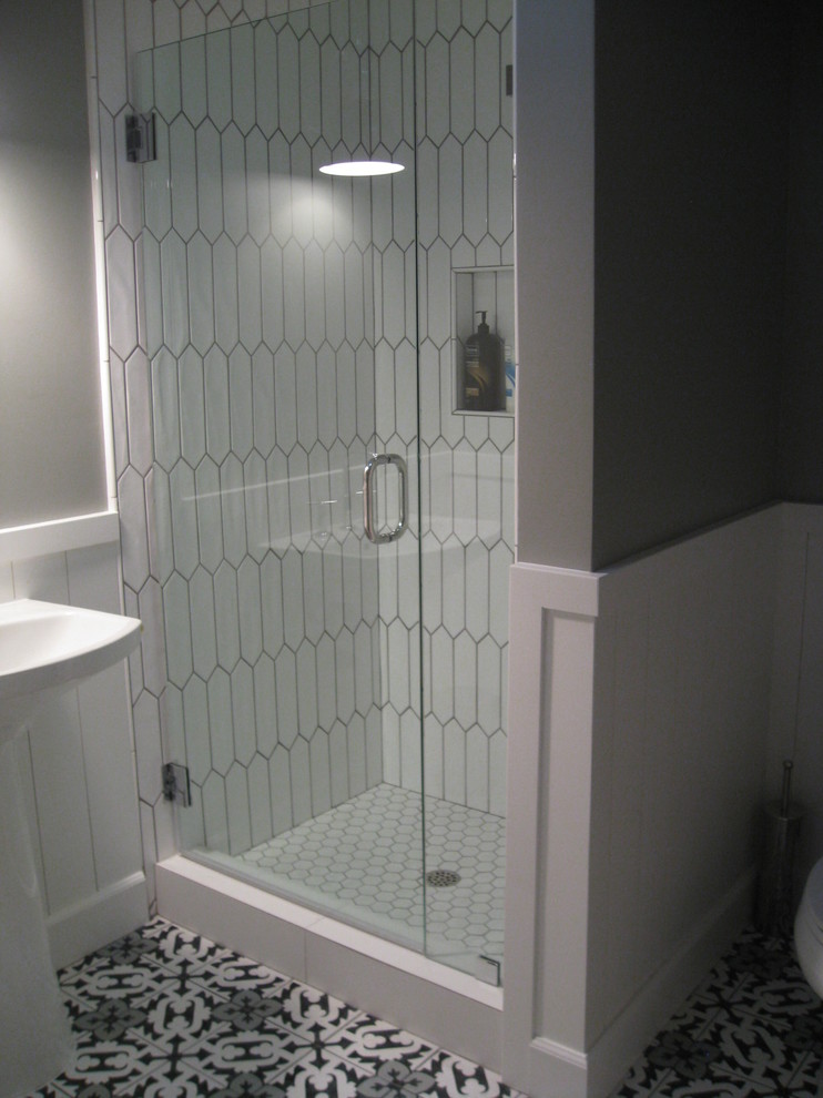 Klassisk inredning av ett mellanstort badrum med dusch, med en dusch i en alkov, en toalettstol med separat cisternkåpa, vit kakel, keramikplattor, grå väggar, ett piedestal handfat, flerfärgat golv och dusch med gångjärnsdörr