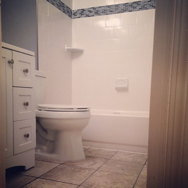 Klassisk inredning av ett litet badrum med dusch, med möbel-liknande, vita skåp, ett badkar i en alkov, en dusch/badkar-kombination, en toalettstol med separat cisternkåpa, svart kakel, blå kakel, grå kakel, grå väggar, klinkergolv i keramik och bänkskiva i kvartsit