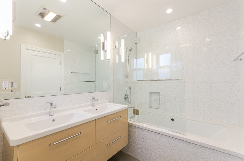 Inredning av ett modernt mellanstort badrum, med ett integrerad handfat, släta luckor, bänkskiva i akrylsten, ett undermonterat badkar, en dusch/badkar-kombination, vit kakel, grå kakel, mosaik, vita väggar, skåp i ljust trä och dusch med gångjärnsdörr