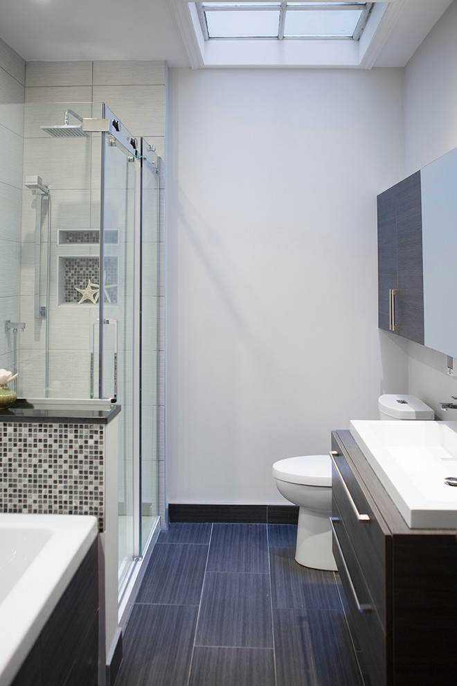 モントリオールにある低価格の小さなコンテンポラリースタイルのおしゃれな浴室 (オーバーカウンターシンク、フラットパネル扉のキャビネット、濃色木目調キャビネット、ラミネートカウンター、アルコーブ型浴槽、コーナー設置型シャワー、一体型トイレ	、モノトーンのタイル、モザイクタイル、グレーの壁、セラミックタイルの床) の写真