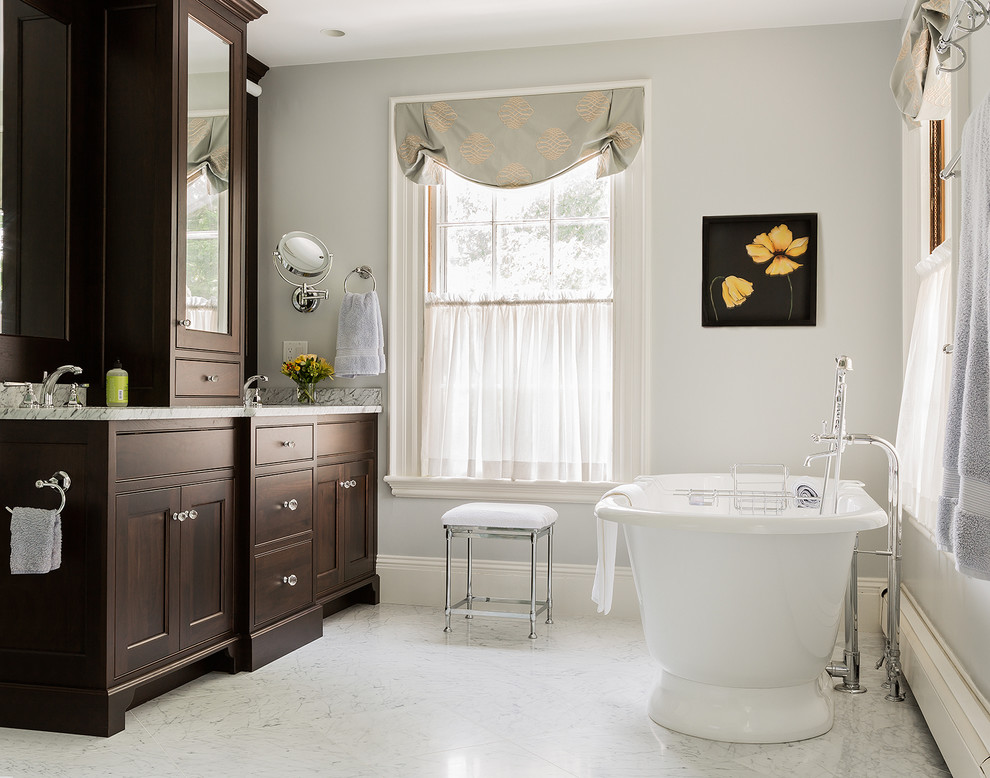 На фото: главная ванная комната в классическом стиле с фасадами с утопленной филенкой, фасадами цвета дерева среднего тона, ванной на ножках, белой плиткой и мраморной столешницей
