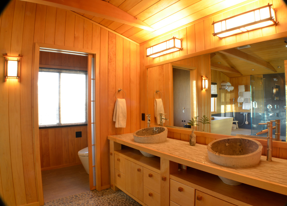 Bild på ett stort orientaliskt en-suite badrum, med släta luckor, skåp i ljust trä, ett fristående badkar, flerfärgad kakel, stenkakel, bruna väggar, klinkergolv i småsten, ett nedsänkt handfat, träbänkskiva och flerfärgat golv