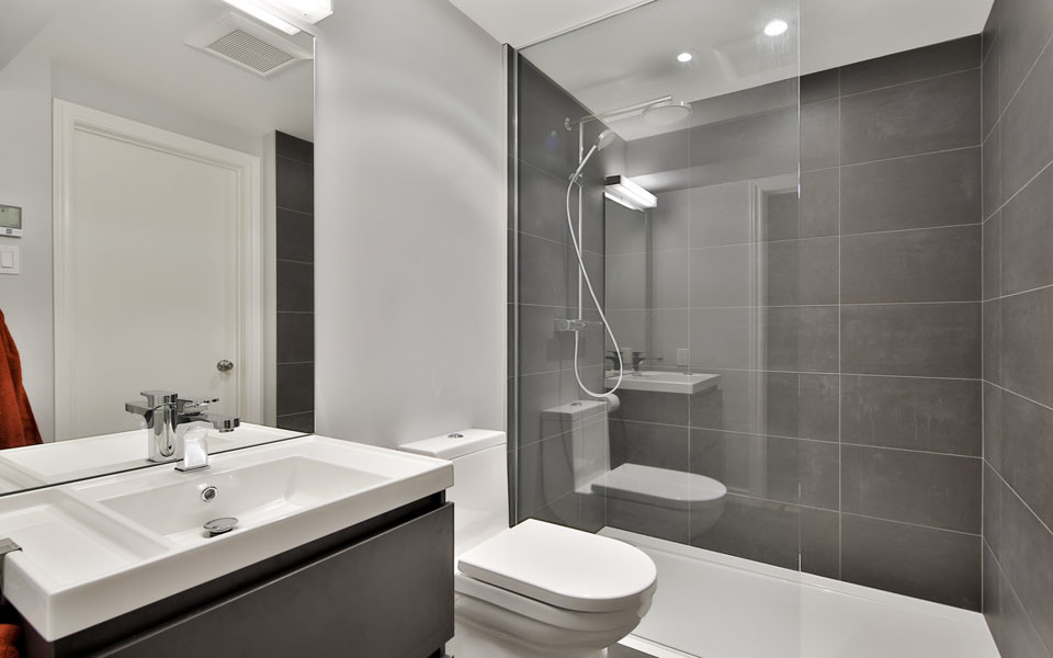 Cette image montre une petite salle de bain design en bois foncé avec un plan vasque, un placard à porte plane, WC à poser, un carrelage gris, des carreaux de porcelaine, un mur gris et un sol en carrelage de porcelaine.