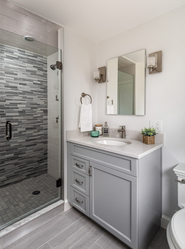 На фото: маленькая главная ванная комната в стиле неоклассика (современная классика) с серыми фасадами, душем в нише, раздельным унитазом, разноцветной плиткой, стеклянной плиткой, серыми стенами, врезной раковиной, столешницей из искусственного кварца, серым полом, душем с распашными дверями, белой столешницей, тумбой под одну раковину, встроенной тумбой и фасадами с утопленной филенкой для на участке и в саду с