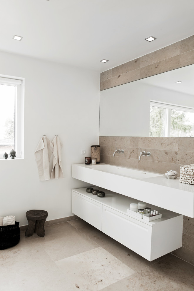 Cette photo montre une salle de bain beige et blanche tendance avec un lavabo intégré, un placard à porte plane, des portes de placard blanches, un carrelage beige, un carrelage de pierre et un mur blanc.