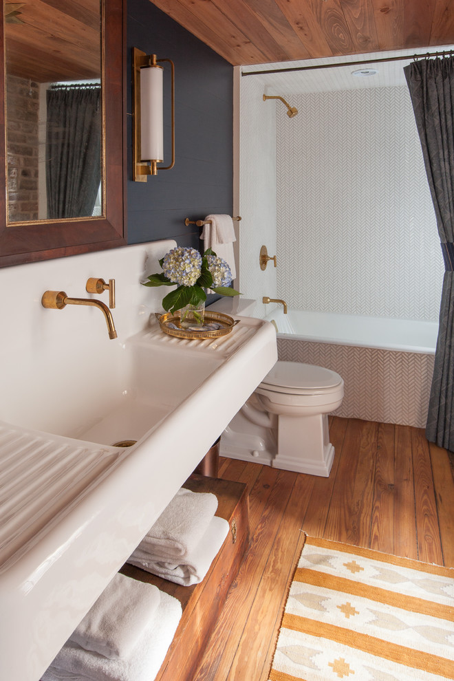 Cette image montre une salle de bain rustique avec une baignoire en alcôve, un combiné douche/baignoire, un carrelage blanc, un mur noir, un sol en bois brun, un lavabo intégré, un sol marron, une cabine de douche avec un rideau et un plan de toilette blanc.