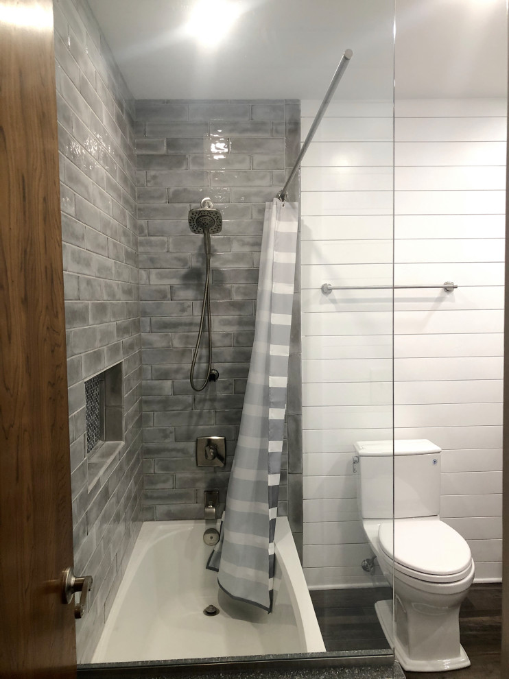 Photo of a medium sized classic family bathroom in Indianapolis with shaker cabinets, medium wood cabinets, an alcove bath, an alcove shower, a two-piece toilet, grey tiles, ceramic tiles, white walls, laminate floors, a submerged sink, engineered stone worktops, grey floors, a shower curtain, white worktops, a wall niche, double sinks, a built in vanity unit and tongue and groove walls.