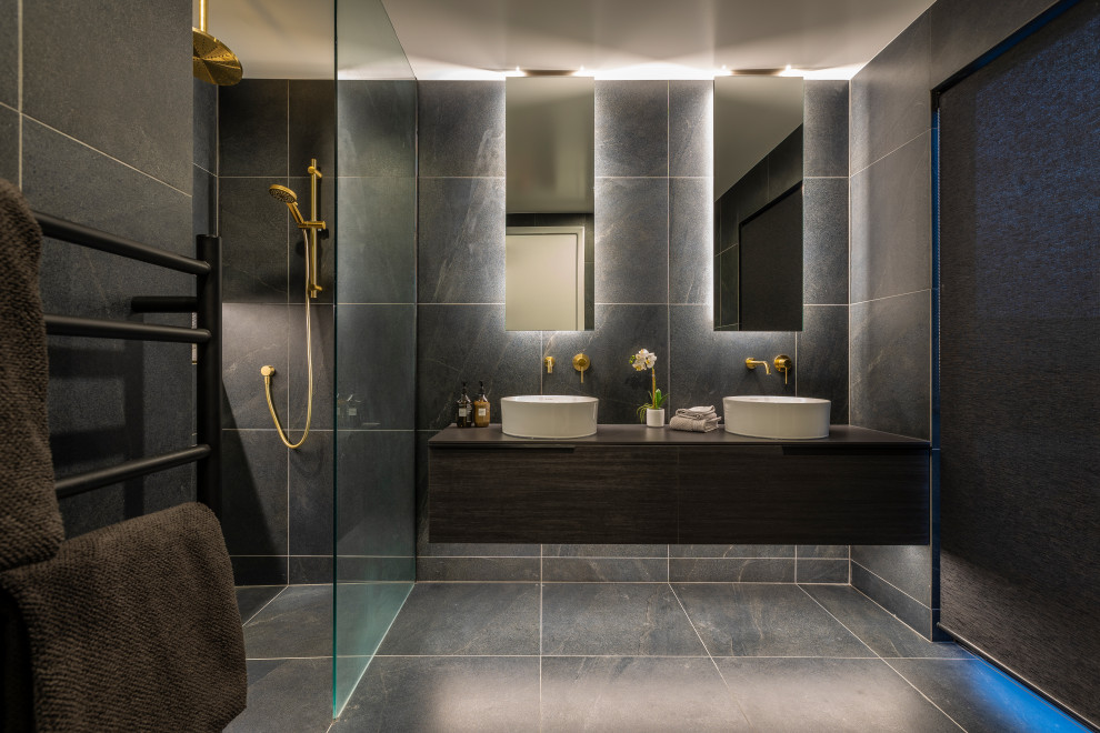 Exemple d'une salle de bain principale tendance en bois foncé de taille moyenne avec un carrelage gris, un plan de toilette noir, meuble double vasque, meuble-lavabo suspendu, un placard à porte plane et un sol gris.