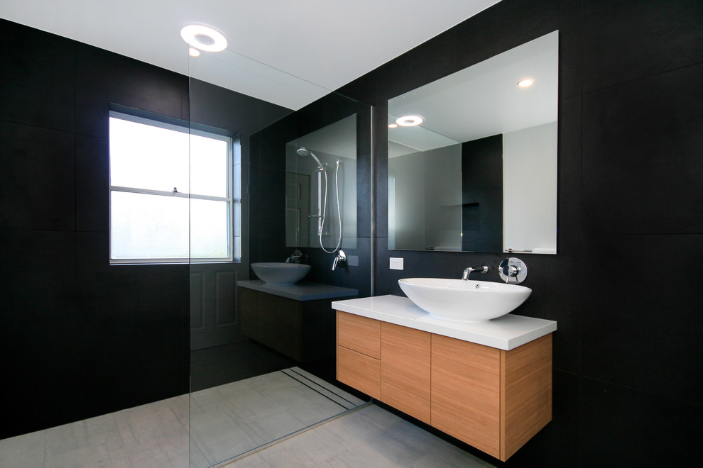 На фото: ванная комната среднего размера в стиле модернизм с угловым душем, унитазом-моноблоком, серой плиткой, керамической плиткой, черными стенами, полом из керамической плитки, душевой кабиной, настольной раковиной и столешницей из искусственного кварца с
