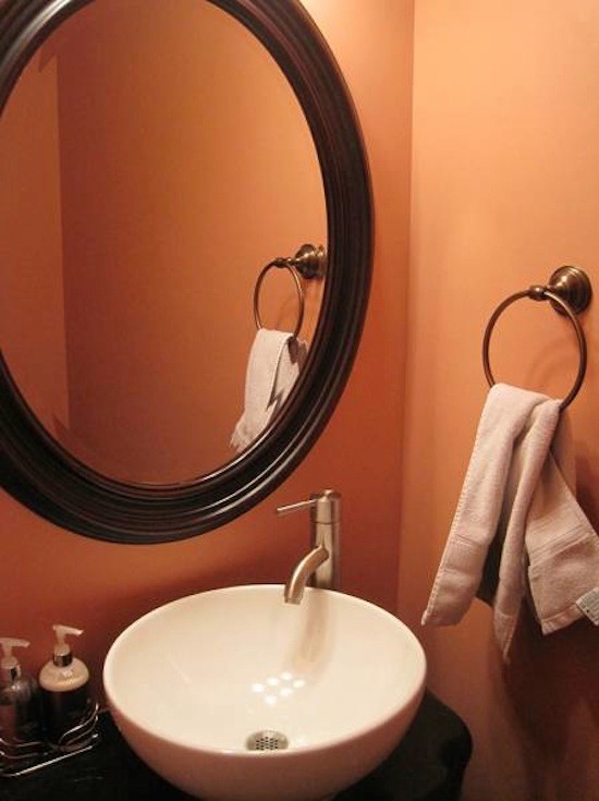 Immagine di una stanza da bagno con lavabo integrato, ante con bugna sagomata, ante in legno bruno e pareti arancioni