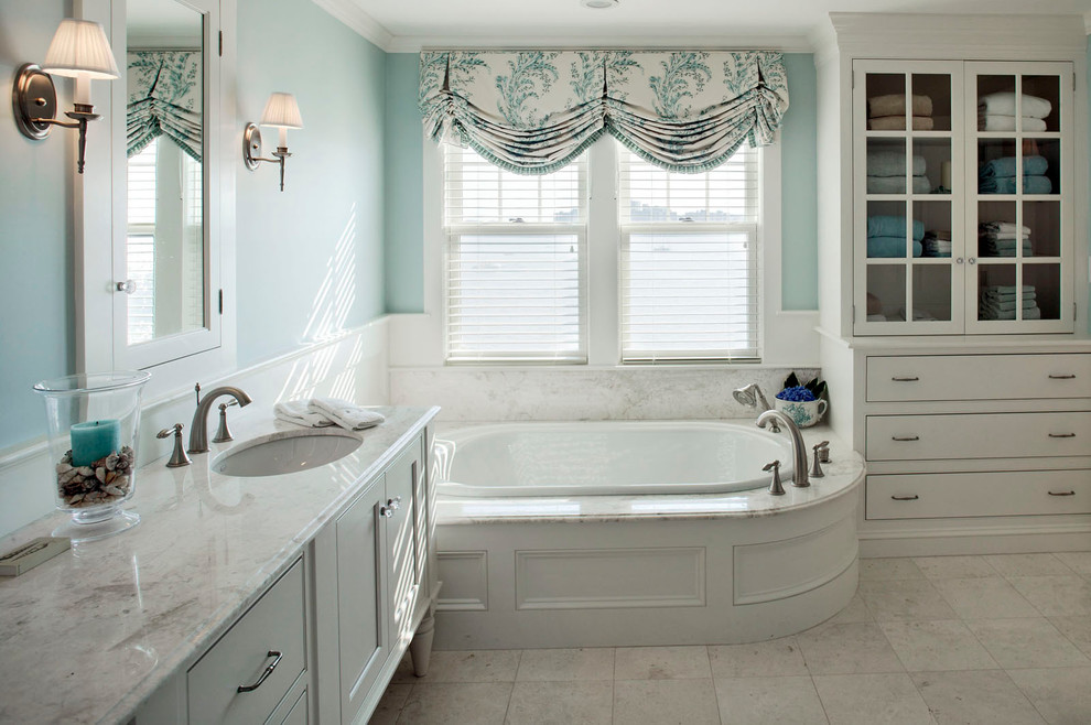 Пример оригинального дизайна: большая главная ванная комната в стиле неоклассика (современная классика) с плоскими фасадами, белыми фасадами, угловым душем, белой плиткой, мраморной столешницей, угловой ванной, плиткой из листового камня, синими стенами, полом из известняка, врезной раковиной и бежевым полом