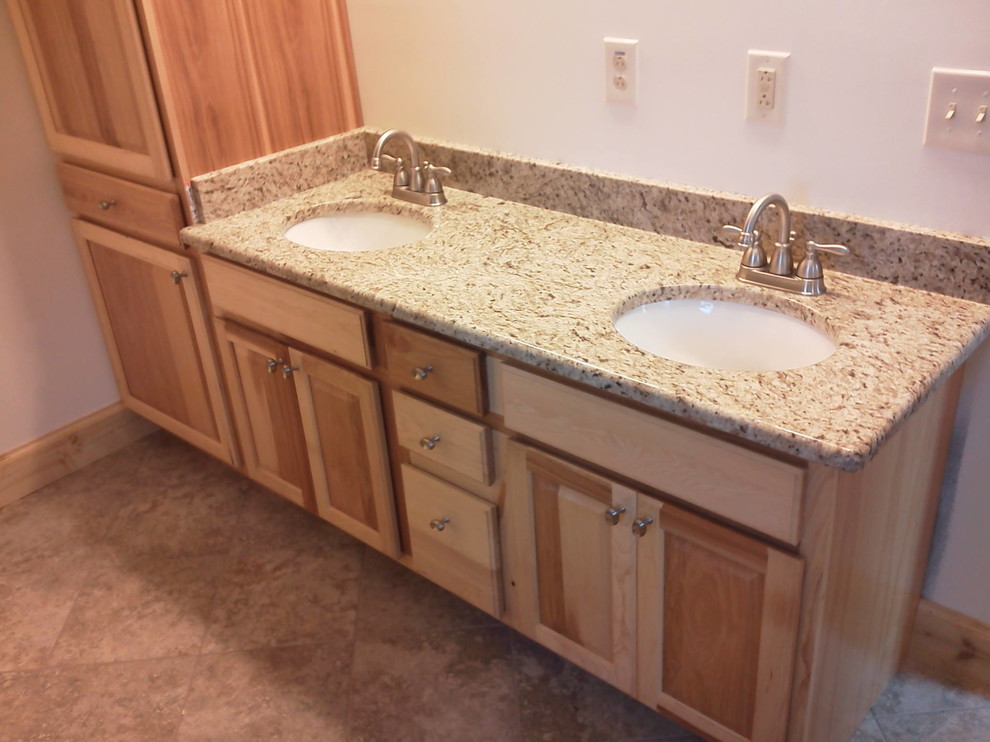 Foto di una stanza da bagno country con ante con bugna sagomata, ante in legno chiaro, lavabo sottopiano e top in granito