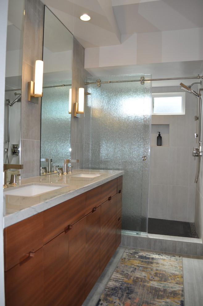 Traditional ensuite bathroom in Los Angeles with flat-panel cabinets, medium wood cabinets, an alcove shower, grey tiles, porcelain tiles, grey walls, porcelain flooring, a submerged sink, engineered stone worktops, grey floors, a sliding door and white worktops.