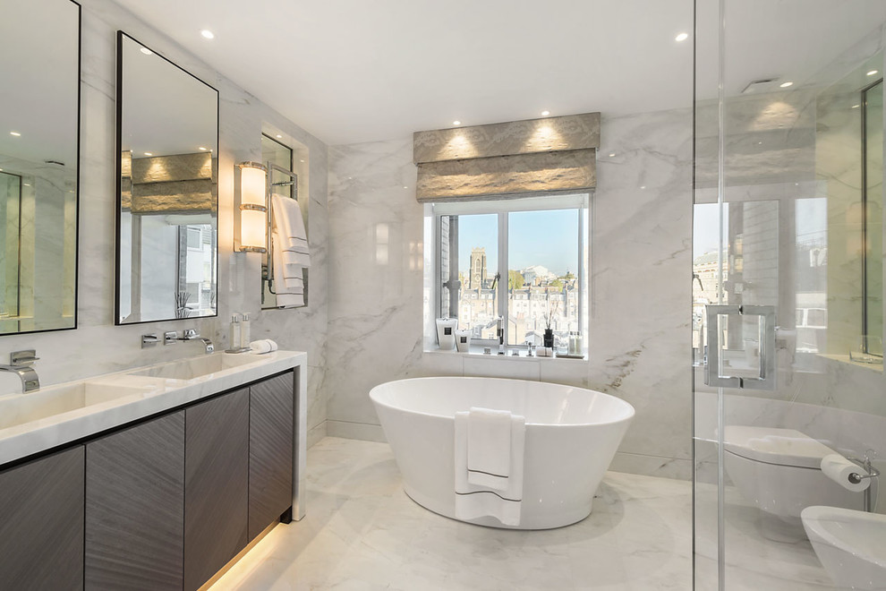 Modern inredning av ett en-suite badrum, med släta luckor, skåp i mörkt trä, ett fristående badkar, en vägghängd toalettstol, marmorgolv, ett integrerad handfat och marmorbänkskiva