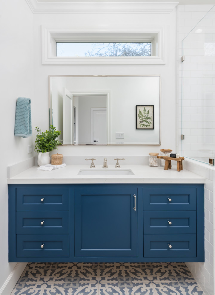 Идея дизайна: ванная комната среднего размера с фасадами с декоративным кантом, синими фасадами, угловым душем, унитазом-моноблоком, белой плиткой, керамической плиткой, белыми стенами, полом из керамической плитки, душевой кабиной, врезной раковиной, столешницей из искусственного кварца, синим полом, душем с распашными дверями и белой столешницей