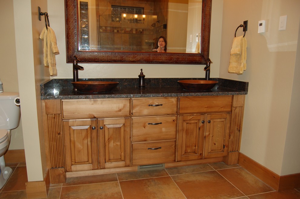 Immagine di una stanza da bagno stile americano con ante con bugna sagomata, ante in legno scuro, lavabo a bacinella e top in granito