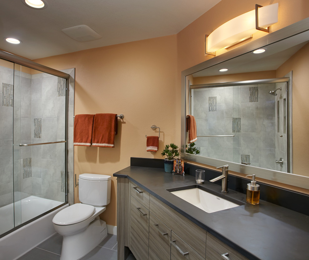 Inspiration for a contemporary gray tile and porcelain tile porcelain tile tub/shower combo remodel in Phoenix with a vessel sink, flat-panel cabinets, gray cabinets, an undermount tub, a two-piece toilet and orange walls