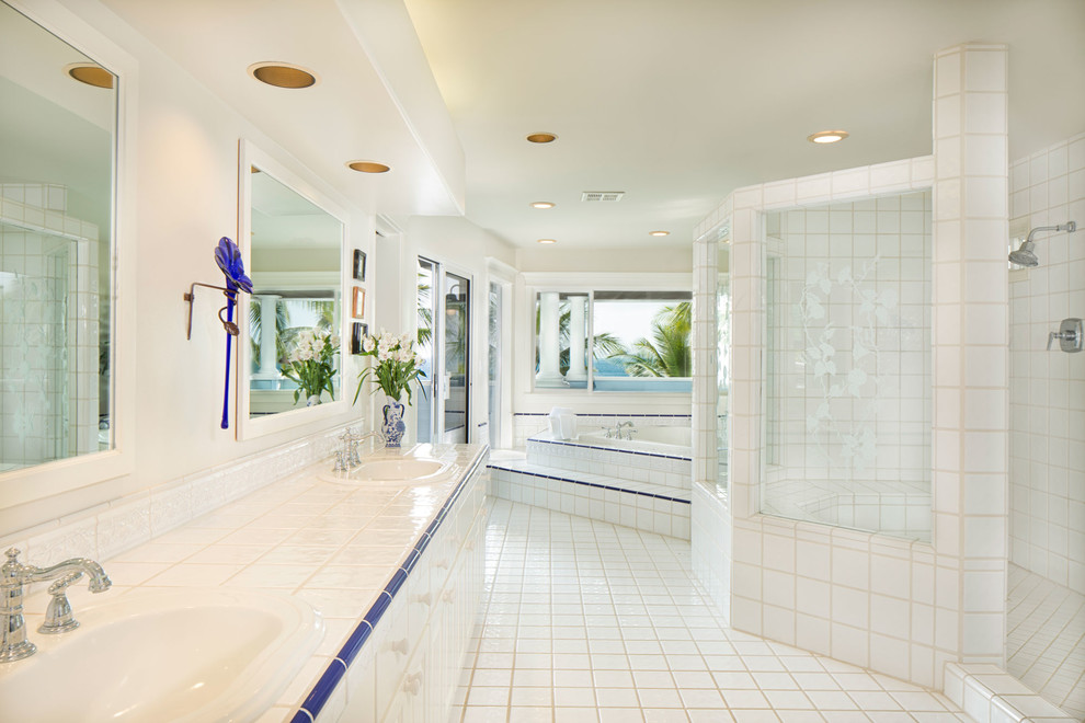 Design ideas for a large coastal ensuite bathroom in Hawaii with flat-panel cabinets, white cabinets, a corner bath, an alcove shower, a one-piece toilet, white tiles, white walls, ceramic flooring, a built-in sink and tiled worktops.