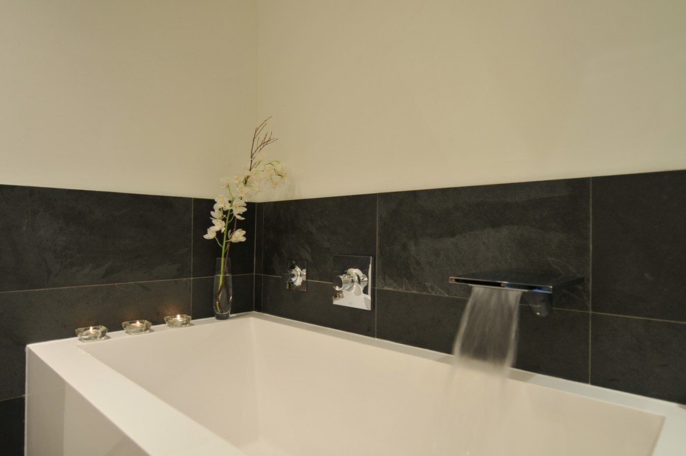 Medium sized contemporary bathroom in Vancouver with a vessel sink, flat-panel cabinets, light wood cabinets, engineered stone worktops, a built-in bath, a corner shower, a two-piece toilet, black tiles, stone tiles, white walls and slate flooring.