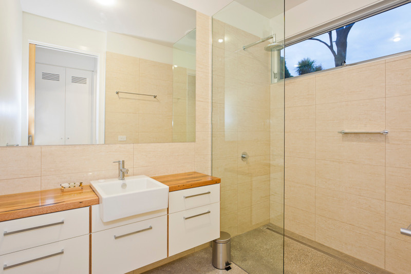 Ejemplo de cuarto de baño contemporáneo con armarios con paneles lisos, puertas de armario blancas, encimera de madera, baldosas y/o azulejos beige y paredes beige
