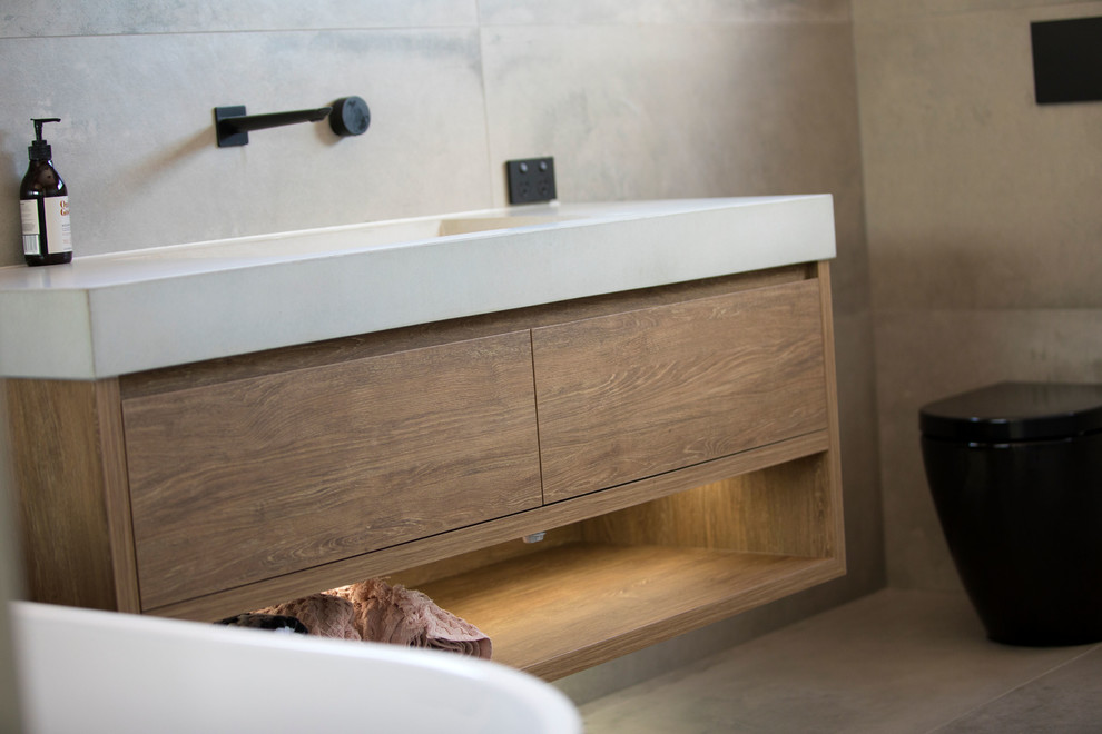 На фото: ванная комната в стиле модернизм с светлыми деревянными фасадами, серой плиткой, раковиной с несколькими смесителями и столешницей из бетона с