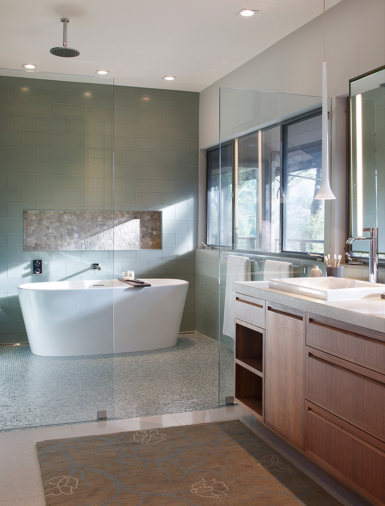 Inredning av ett modernt en-suite badrum, med släta luckor, skåp i mellenmörkt trä, ett nedsänkt handfat, ett fristående badkar, en dusch/badkar-kombination, blå kakel, glaskakel och grå väggar