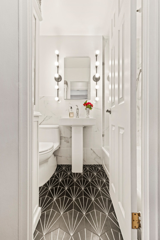 Modern inredning av ett litet badrum med dusch, med en toalettstol med hel cisternkåpa, vita väggar, svart golv, ett badkar i en alkov, en dusch/badkar-kombination, ett piedestal handfat, med dusch som är öppen, vit kakel och marmorkakel