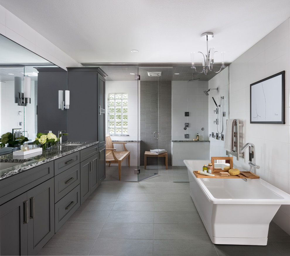 Klassisk inredning av ett en-suite badrum, med ett fristående badkar, en kantlös dusch, bänkskiva i kvarts, grått golv, dusch med gångjärnsdörr, skåp i shakerstil, grå skåp, grå kakel, flerfärgad kakel, vit kakel, grå väggar och ett undermonterad handfat
