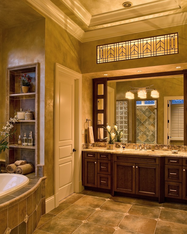 Cette photo montre une grande salle de bain principale chic en bois foncé avec un lavabo encastré, un placard avec porte à panneau encastré, une baignoire posée, des carreaux de céramique, un mur beige, un plan de toilette en granite et un carrelage marron.