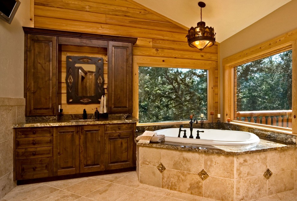 Cette image montre une grande salle de bain principale chalet en bois foncé avec un placard avec porte à panneau surélevé, une baignoire posée, WC séparés, un carrelage beige, un mur beige, un lavabo encastré et un plan de toilette en granite.