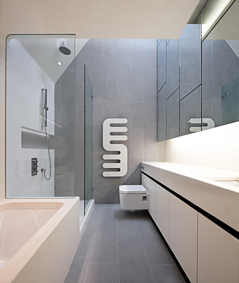 Design ideas for a medium sized contemporary family bathroom in London with flat-panel cabinets, white cabinets, solid surface worktops, grey tiles, a built-in bath, ceramic tiles, a walk-in shower, a wall mounted toilet, a built-in sink, white walls and ceramic flooring.