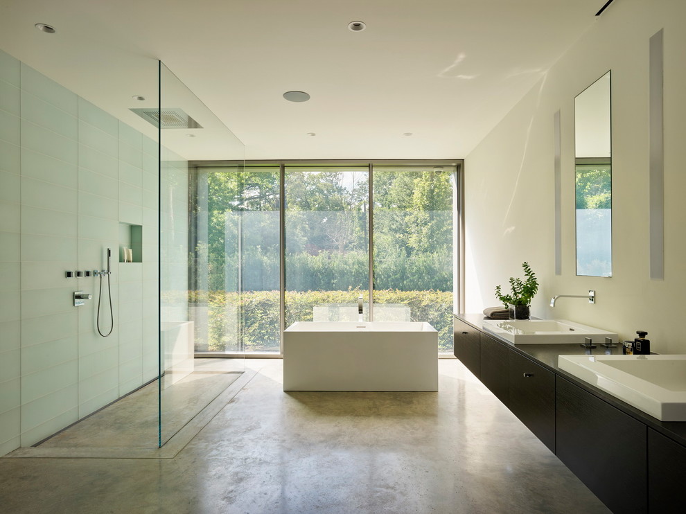 На фото: ванная комната в стиле модернизм с плоскими фасадами, темными деревянными фасадами, отдельно стоящей ванной, синей плиткой, стеклянной плиткой, белыми стенами, бетонным полом, накладной раковиной, серым полом и коричневой столешницей с