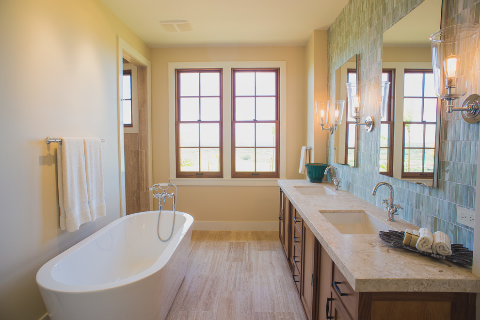 Esempio di una stanza da bagno tropicale con lavabo sottopiano, ante in legno bruno, vasca freestanding, piastrelle blu, piastrelle a mosaico, pareti beige e vasca/doccia