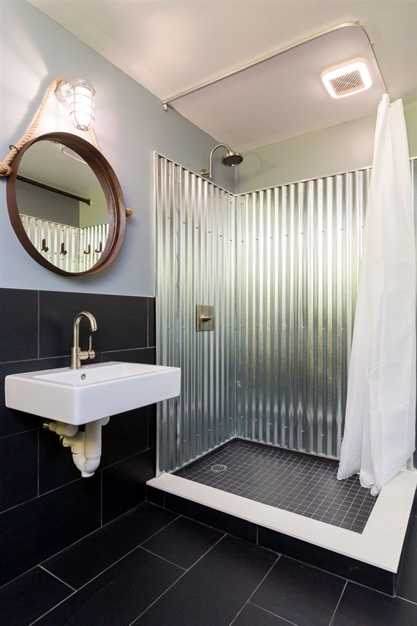Inredning av ett industriellt mellanstort badrum, med en öppen dusch, en vägghängd toalettstol, svart kakel, porslinskakel, ett väggmonterat handfat, klinkergolv i porslin och grå väggar
