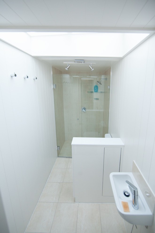 Lantlig inredning av ett litet badrum, med vita skåp, en dubbeldusch, en toalettstol med hel cisternkåpa, vit kakel och vita väggar